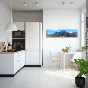 May include: A panoramic photograph of a city nestled in a valley surrounded by mountains. The photo is printed on canvas and framed in a white frame. The photo is hanging on a white wall in a modern kitchen.