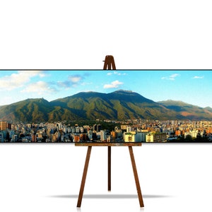 May include: A panoramic view of a city nestled at the foot of a mountain range. The city is a mix of modern and traditional buildings, with a lush green mountain in the background. The sky is a bright blue with fluffy white clouds.
