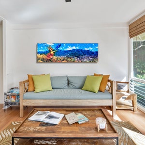 May include: A colorful abstract painting of a parrot flying over a mountain range with a city in the background. The painting is framed and hanging on a white wall in a living room.