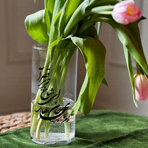 May include: A clear glass vase with a black calligraphy design on the side. The vase is filled with water and green tulips.