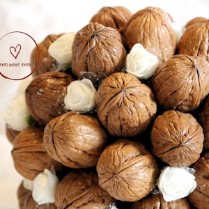 May include: A bouquet of walnuts arranged in a circular shape, decorated with white fabric roses. The walnuts are brown and have a rough texture.