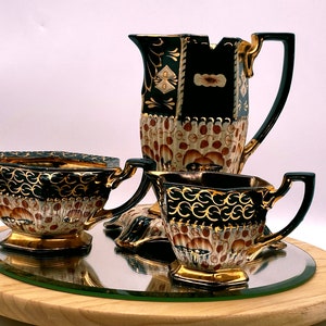 May include: A black and gold tea set with a pitcher, creamer, and sugar bowl. The set has a floral pattern and is decorated with gold accents.