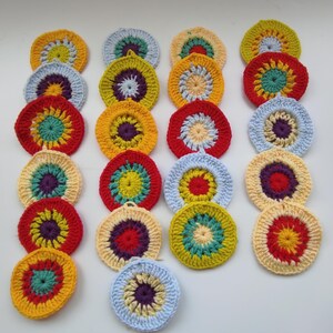 May include: A collection of colorful, crocheted circular coasters. Each coaster features a vibrant, concentric design with a variety of colors including yellow, red, blue, and purple. The handmade coasters are arranged on a white surface.