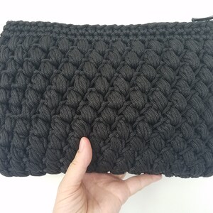 Può includere: Una pochette nera all'uncinetto con chiusura a zip. La borsa è realizzata con un punto testurizzato e gonfio.