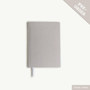 Puede incluir: Un cuaderno gris claro con una cubierta texturizada y un marcap&aacute;ginas de cinta blanca. La cubierta tiene un sutil patr&oacute;n de rayas. El cuaderno est&aacute; etiquetado como "PRE-ORDER" en la esquina superior derecha.  Portada.