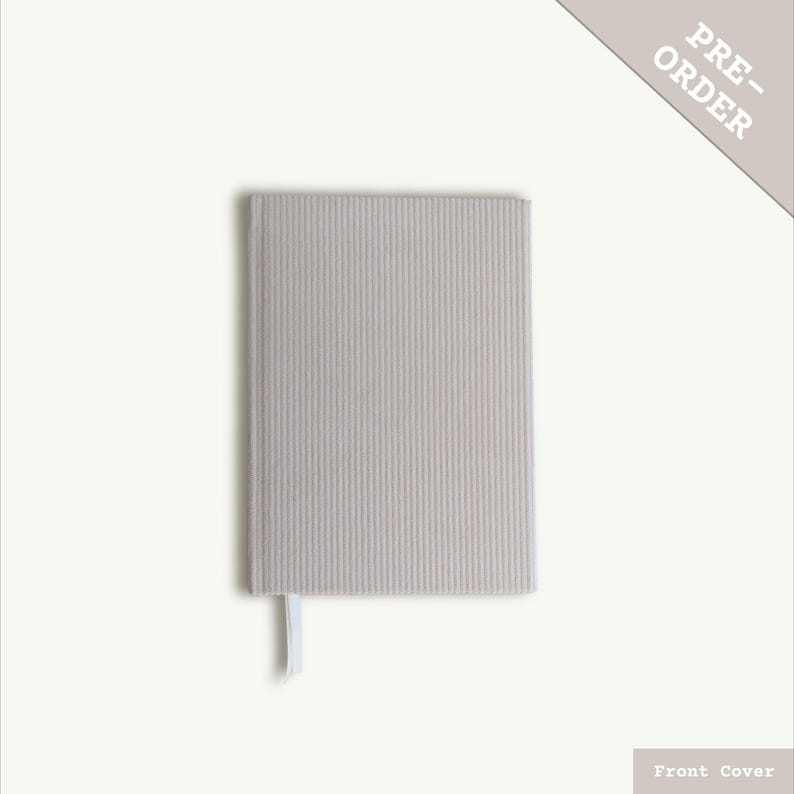 Puede incluir: Un cuaderno gris claro con una cubierta texturizada y un marcap&aacute;ginas de cinta blanca. La cubierta tiene un sutil patr&oacute;n de rayas. El cuaderno est&aacute; etiquetado como "PRE-ORDER" en la esquina superior derecha.  Portada.