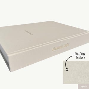 K&ouml;nnte beinhalten: Ein hellgraues Hardcover-Journal mit dem in Gold gepr&auml;gten Text "Living in Light" auf dem R&uuml;cken. Der Einband hat eine dezente, strukturierte Oberfl&auml;che.