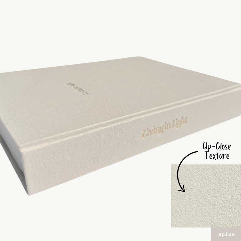 K&ouml;nnte beinhalten: Ein hellgraues Hardcover-Journal mit dem in Gold gepr&auml;gten Text "Living in Light" auf dem R&uuml;cken. Der Einband hat eine dezente, strukturierte Oberfl&auml;che.