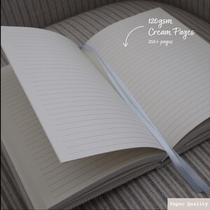 Puede incluir: Cuaderno abierto con p&aacute;ginas de color crema y papel rayado. El cuaderno tiene un marcador de cinta y el texto "120gsm Cream Pages 250+ pages" es visible en la p&aacute;gina derecha.