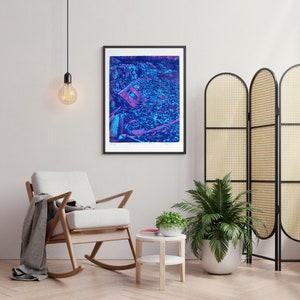 Pode incluir: Uma impressão artística emoldurada apresentando uma paisagem abstrata de alto contraste em tons de azul profundo, magenta e violeta. A composição exibe um terreno rochoso texturizado com detritos espalhados e um elemento de moldura retangular, tudo renderizado em cores vibrantes e saturadas.