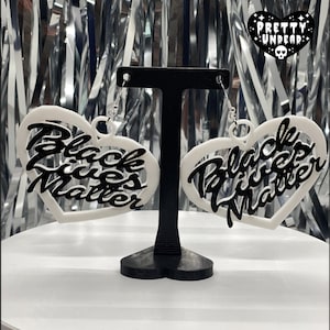 May include: White heart-shaped earrings with the phrase "Black Lives Matter" written in black lettering.
