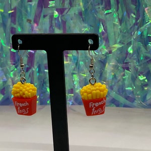 May include: A pair of dangle earrings featuring a red and yellow french fries charm with the text "French Fries".