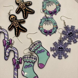 Puede incluir: Un conjunto de 10 pendientes de Navidad espeluznantes con una variedad de dise&ntilde;os, que incluyen una ca&ntilde;a de az&uacute;car, una media, un copo de nieve, una corona y un esqueleto. Los pendientes est&aacute;n hechos de pl&aacute;stico y tienen una combinaci&oacute;n de colores p&uacute;rpura, verde y negro.