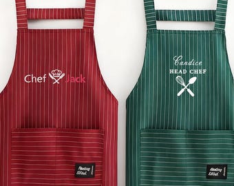 May include: Two striped aprons hanging on a wall. One is burgundy with white stripes and the text "Chef Jack". The other is green with white stripes and the text "Candice HEAD CHEF". Both have a front pocket and a small label.