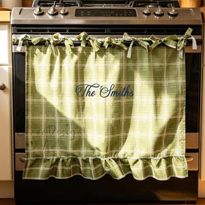Peut inclure: Jupe de cuisinière à carreaux verts avec des accents blancs et un ourlet à volants. Le tissu est attaché à la cuisinière avec des liens verts et blancs assortis. Le texte "The Smiths" est brodé sur la jupe.