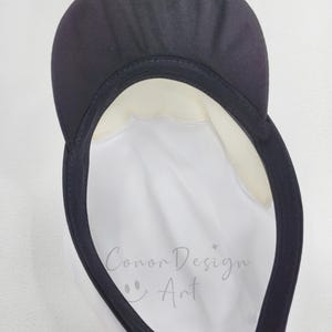 May include: A white cap with a black brim and a black interior sweatband. The interior crown features the text "Conor Design Art" printed in a light gray script font, accompanied by a small smiley face icon and a four-pointed star symbol.