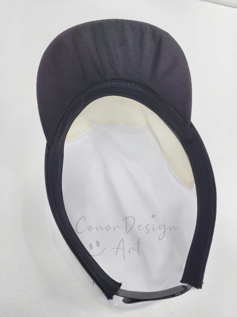 May include: A white cap with a black brim and a black interior sweatband. The interior crown features the text "Conor Design Art" printed in a light gray script font, accompanied by a small smiley face icon and a four-pointed star symbol.