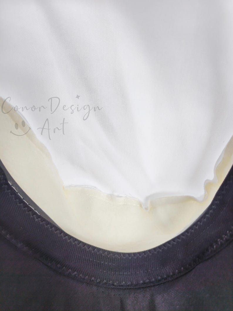 May include: A white fabric layer overlapping a cream-colored section, bordered by a black trim with visible stitching. The text 'Conor Design Art' with a small smiley face icon is printed in a light gray script on the white fabric surface.
