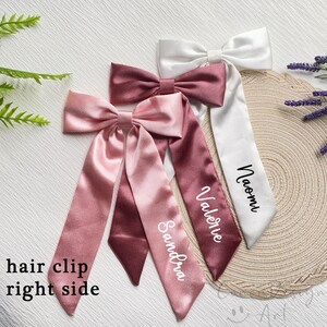 May include: Satin hair clips in shades of pink and white, each with a bow and long streamers. The streamers are personalized with names in elegant script. The text "hair clip right side" is visible.