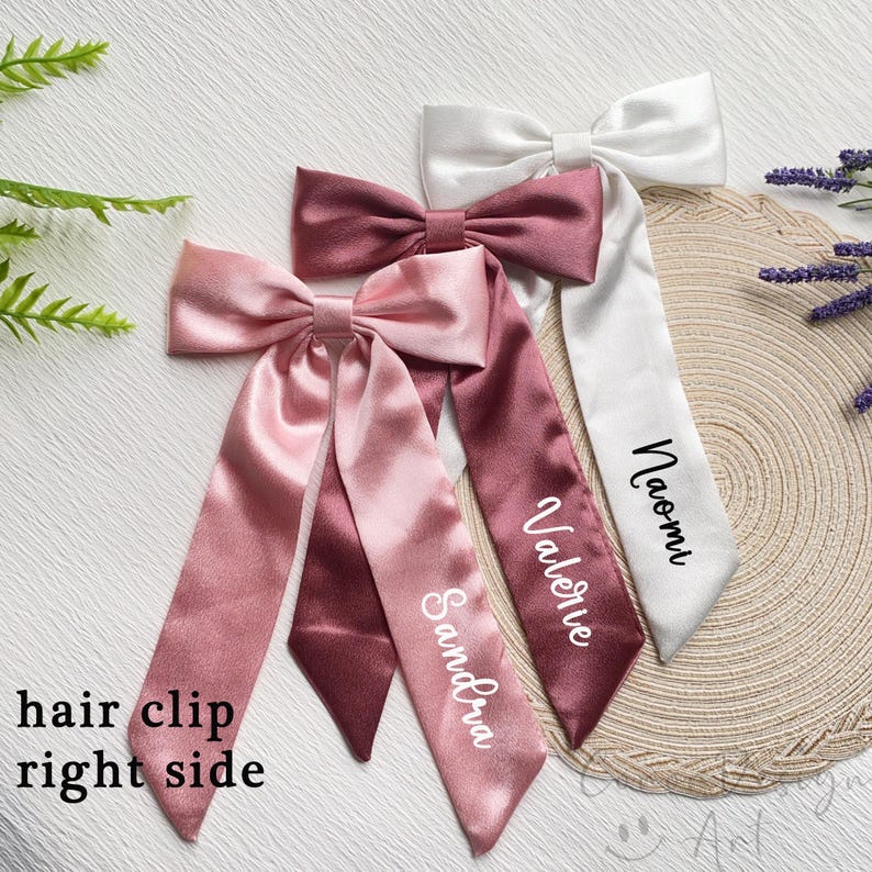 May include: Satin hair clips in shades of pink and white, each with a bow and long streamers. The streamers are personalized with names in elegant script. The text "hair clip right side" is visible.