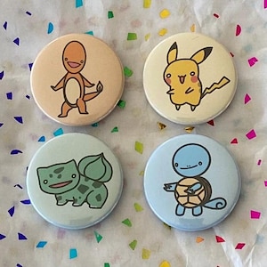 Peut inclure: Quatre boutons ronds et colorés avec des images de personnages de Pokemon en dessin animé. Les boutons représentent Bulbizarre, Carapuce, Salamèche et Pikachu.