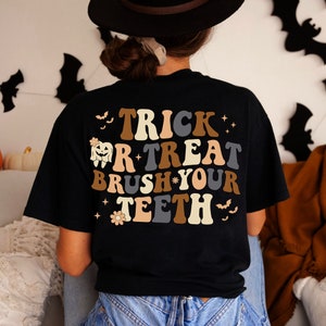 May include: Black t-shirt with a retro-style graphic that says "Trick or Treat Brush Your Teeth" with a tooth and flower design.