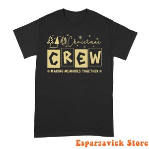 May include: A black short-sleeved t-shirt featuring a gold graphic design. The text reads Christmas CREW MAKING MEMORIES TOGETHER, accompanied by illustrations of pine trees and snowflakes. The design is centered on the front of the shirt.