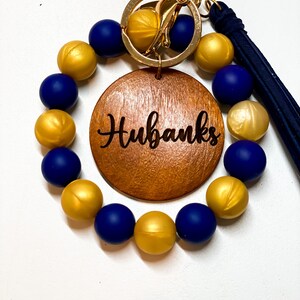 Peut inclure: Un bracelet en perles bleu marine et dor&eacute;es avec un charme en bois qui dit "Hubanks" et un porte-cl&eacute;s dor&eacute; attach&eacute;.