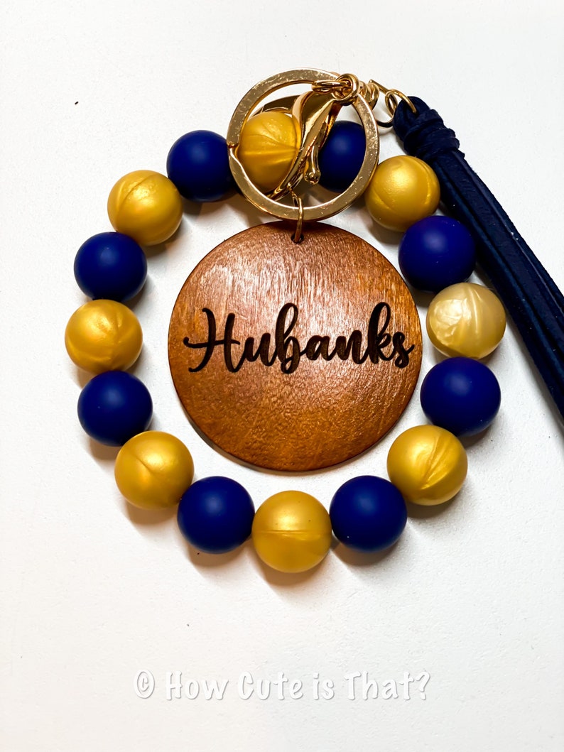 Peut inclure: Un bracelet en perles bleu marine et dor&eacute;es avec un charme en bois qui dit "Hubanks" et un porte-cl&eacute;s dor&eacute; attach&eacute;.