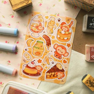 May include: A rectangular sticker sheet featuring various illustrations of monkeys, bananas, and banana-themed desserts. The designs include a monkey in a parfait, a chocolate-covered banana, a banana milk carton with Korean text, and a slice of cake.