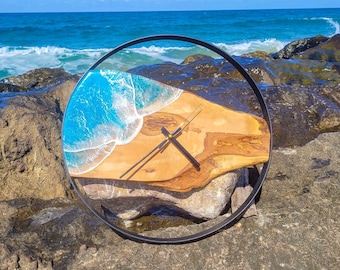 May include: A round wooden clock with a blue and white resin wave design. The clock is set against a backdrop of rocks and ocean waves.
