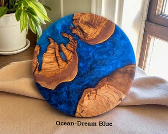 Puede incluir: Tabla redonda de madera para servir con un vibrante centro de resina azul, con patrones naturales de vetas de madera. La tabla está etiquetada como "Ocean-Dream Blue". Esta pieza decorativa es ideal para servir aperitivos o como un acento de decoración del hogar único.