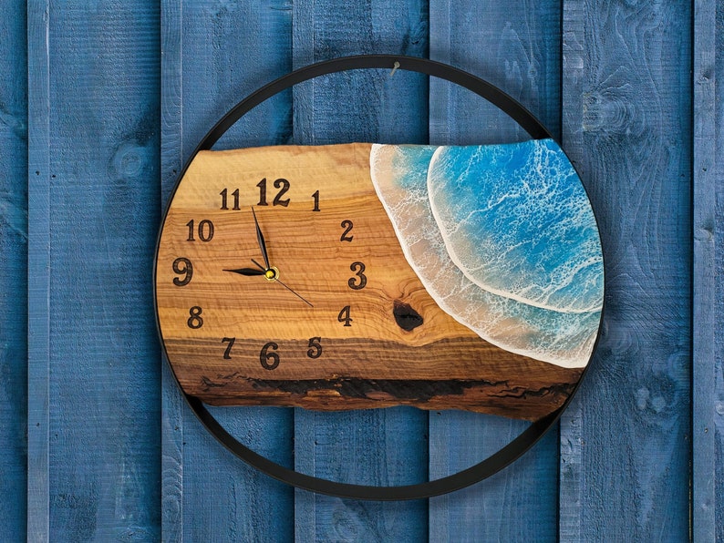 Pu&ograve; includere: Un orologio in legno con cornice in metallo nero, che presenta un design a onda in resina blu e bianca. Il quadrante dell'orologio ha numeri e lancette neri.