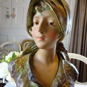 May include: A ceramic bust of a woman with a brown and green patterned scarf. The bust is painted in shades of brown, green, and white.