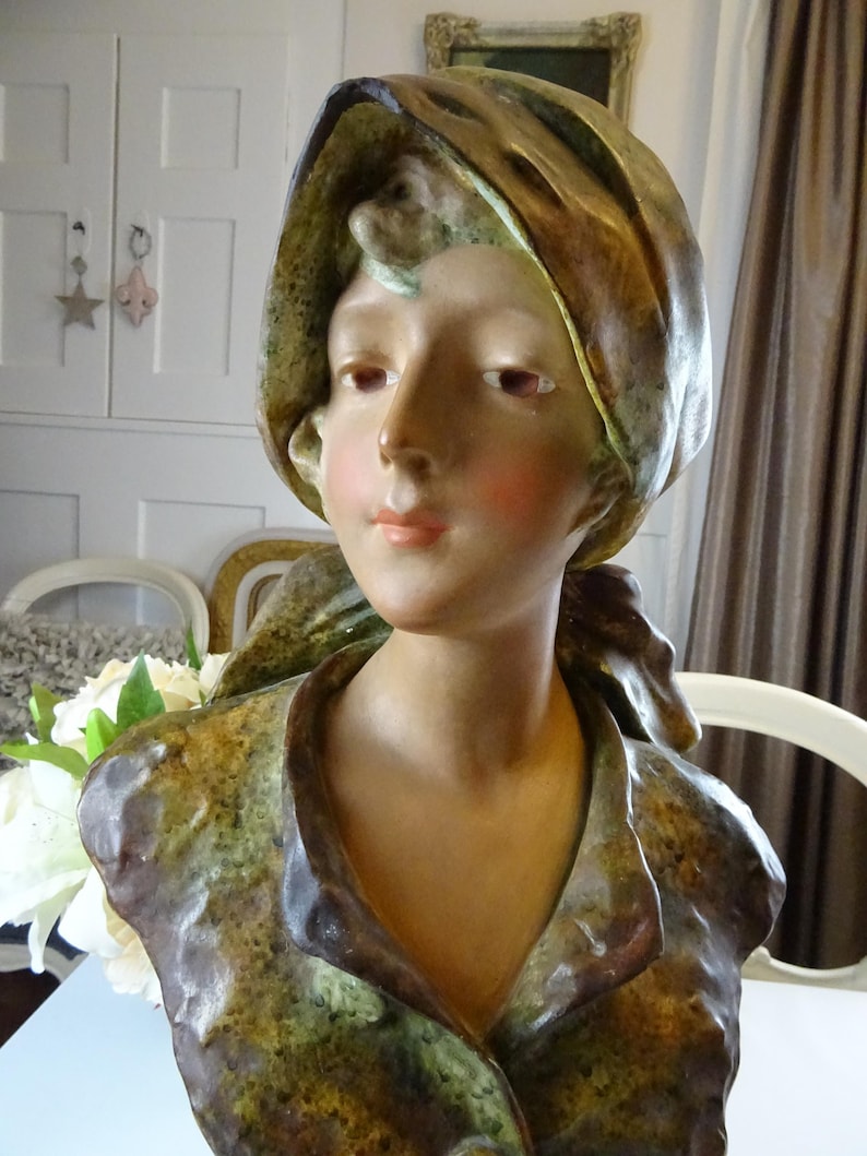 May include: A ceramic bust of a woman with a brown and green patterned scarf. The bust is painted in shades of brown, green, and white.