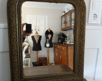 May include: A large, ornate, gold-painted, wooden mirror with a bevelled glass mirror. The mirror is framed with a decorative, carved, floral design. The mirror is hanging on a wall.