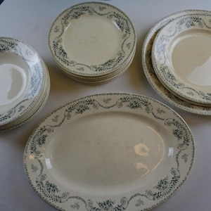Könnte beinhalten: Ein Set vintage weißer Keramikteller mit grünem Blumendesign. Das Set beinhaltet eine große ovale Platte, ein Set Speiseteller und ein Set Suppenschalen.