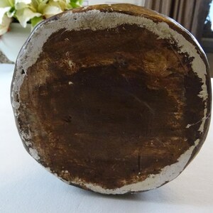 May include: The bottom of a brown ceramic vase with a white rim. The vase has a rough, textured surface.