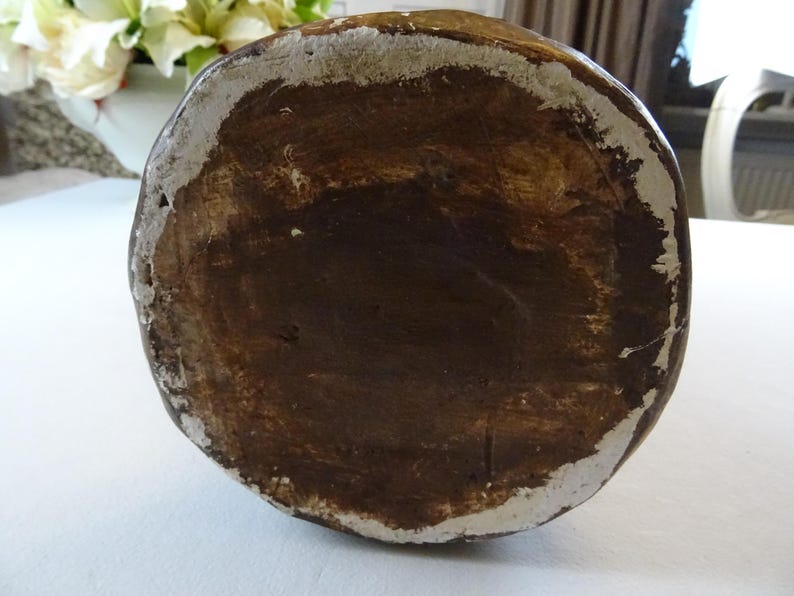 May include: The bottom of a brown ceramic vase with a white rim. The vase has a rough, textured surface.