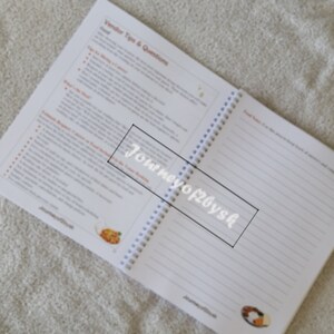 May include: An open spiral bound notebook with white pages and a white cover. The cover has the text "Journey of 20ys" printed in black.