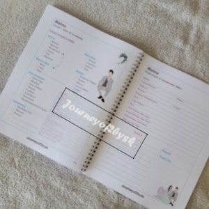 May include: A white and blue wedding planner with a spiral binding. The planner has sections for "Wedding", "Ceremony & Reception", and "Details". The cover features a cartoon illustration of a couple in wedding attire.