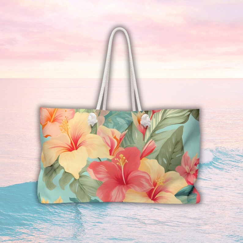 May include: A large, floral tote bag with a white handle. The bag features a tropical print with pink, yellow, and green hibiscus flowers on a light blue background.