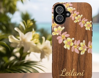 May include: A wooden phone case featuring a floral design with pink and yellow flowers. The case has the name "Leilani" in gold script. The background shows a beach scene with white flowers.