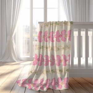 May include: A pink and white floral baby blanket with a repeating pattern of pink flowers and white leaves. The blanket is draped over a white crib.