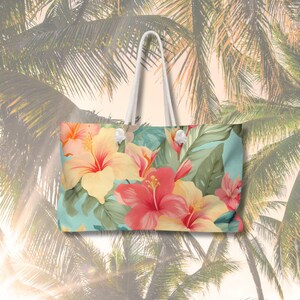 May include: A white tote bag with a tropical floral print featuring pink, yellow, and green hibiscus flowers on a light blue background.