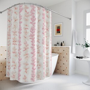 Op de afbeelding: Een wit douchegordijn met een roze bloemenpatroon. Het gordijn heeft een gebogen stang en hangt in een badkamer.