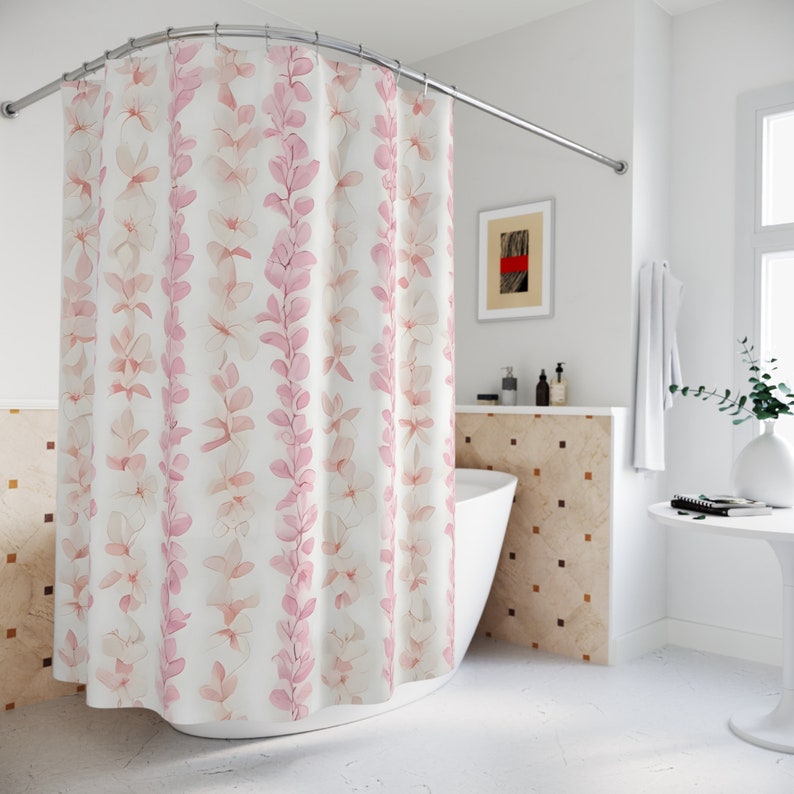Op de afbeelding: Een wit douchegordijn met een roze bloemenpatroon. Het gordijn heeft een gebogen stang en hangt in een badkamer.