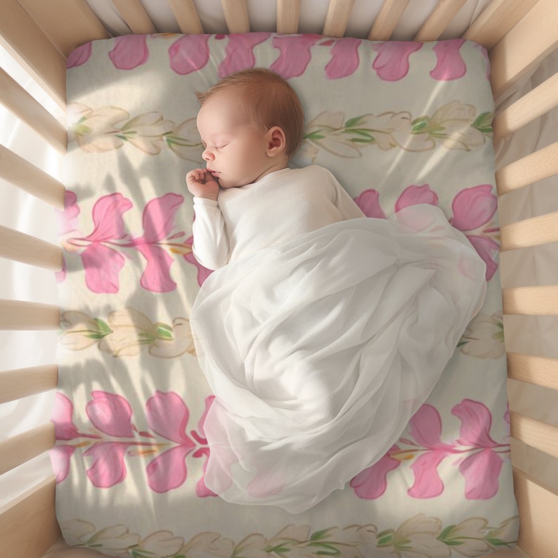 May include: A baby sleeping in a crib with a pink floral patterned sheet. The baby is wearing a white onesie and is swaddled in a white blanket.
