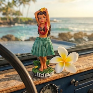 May include: A vintage dashboard features a hula girl figurine with a green skirt and lei, and a white and yellow plumeria flower. The figurine is on a base that says "Hawaii". The background shows a beach and ocean.