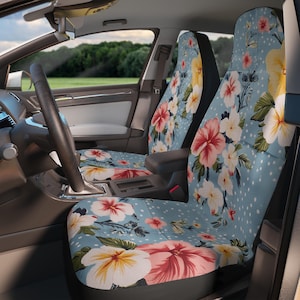 May include: Car seat covers with a floral design. The covers have a light blue backdrop with white polka dots and large flowers in shades of pink, red, and yellow. The car interior includes a steering wheel and dashboard.